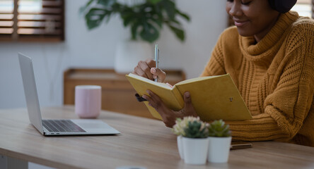 Young African woman holding a book with earphones sitting on sofa at home, young woman stay at home concept.