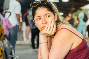 young latin woman waiting sitting on the street, with her hand on her face with a bored expression