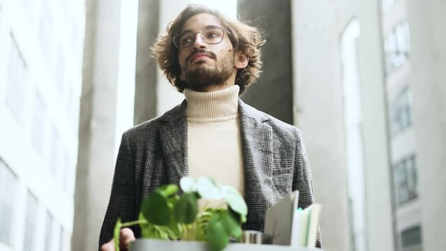 Portrait of fired sad young arabian businessman carries his box with personal belongings leaving the office centre Pensive muslim man with glasses thinking about future after unemployed  outdoors