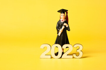 Class of 2023 concept. Wooden number 2023 with graduate statuette on color background