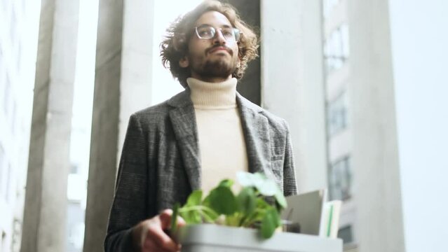 Portrait of fired sad young arabian businessman carries his box with personal belongings leaving the office centre Pensive muslim man with glasses thinking about future after unemployed outdoors