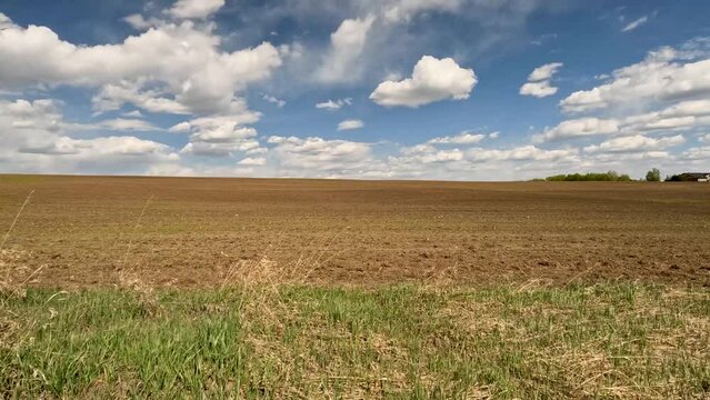 Tilled dirt field with white puffy clouds in a blue sky in a rural setting