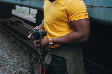 A young man of African African appearance in a bright yellow t-shirt holds a SLR camera in his...