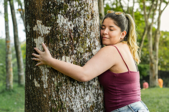 beautiful latina girl, environmentalist, tenderly hugging the trunk of a large tree in a park.