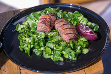 ready to eat - lamb's lettuce, red onions and roasted meat from a red deer calf on a black plate