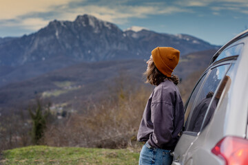 Young woman traveler standing near car watching a beautiful mountain view while travel driving road...