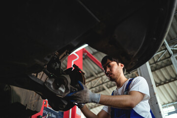 Auto mechanic in the service center. Asian male mechanical engineer working under vehicle in car service repair specialist maintenance technician.