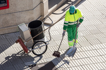 Street sweeper working on a sidewalk with her shovel, trolley and broom