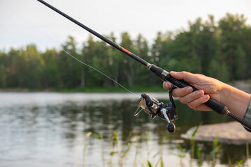 Close up of a man's hand holding a fishing rod. Sunset soft light, selective focus, blurred forest...