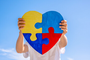 Boy hands holding colorful jigsaw puzzle heart over blue sky background. World autism awareness...