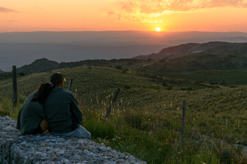 Fototapeta premium Pareja enamorada mirando el atardecer en la montaña. Sensación de libertad, calma y armonía. 