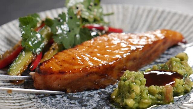 Tasty baked salmon steak being served on plate with herbs and vegetable susing culinary tongs. Slow motion. delicious food. Luxury restaurant. roasted salmon fillet. Full hd