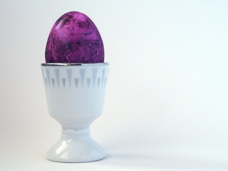 Purple Easter egg in a white egg stand on a white background
