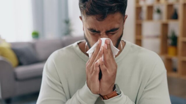 Covid, blowing nose and allergies with a man in his home feeling sick, ill or unwell in the living room. Healthcare, tissue and sneezing with a young male suffering from a virus infection in a house