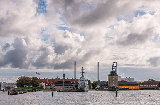 Copenhagen, Denmark - September 13, 2010: Navy museum area on east shore of harbor with F352 HDMS Peder Skram fregate bow, historical crane tower, chimneys and buildings. Blue cloudscape