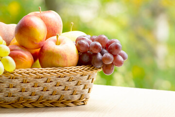Fresh ripe apples, peaches, green and blue grapes in basket. Healthy food on table on defocus autumn background.