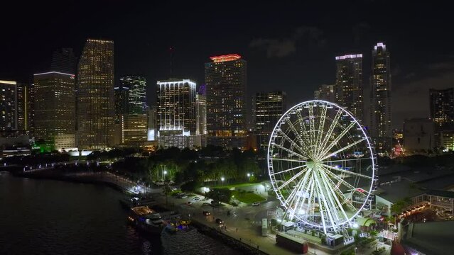 Skyviews Miami Observation Wheel at Bayside Marketplace with reflections in Biscayne Bay water and high illuminated skyscrapers of Brickell, city's financial center. US urban landscape at night