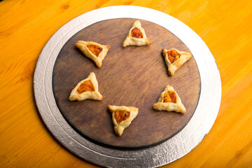 Triangular gomentashi cookies for the holiday of Purim on a blackboard are laid out on a round board on a light table.