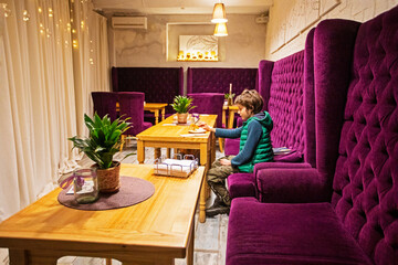 boy in a green vest eats a cake in a modern stylish interior with purple chairs and wooden tables with a green flower