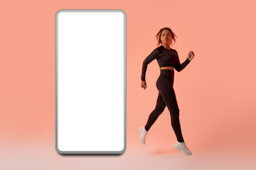 Fitness app. Black woman jumping or running from smartphone with blank screen, neon peach studio background, mockup