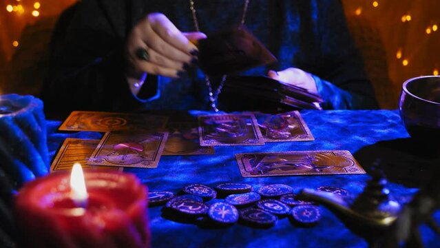 A fortune teller at a table in candlelight reads the future from tarot cards on black velvet with blue highlights. Medium plan.
