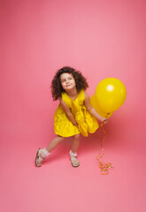Fototapeta na wymiar Portrait of a cheerful little girl isolated on a pink background, holding a bunch of colorful balloons, posing.
