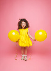 Portrait of a cheerful little girl isolated on a pink background, holding a bunch of colorful balloons, posing.