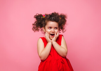 emotional portrait of a little girl in a red dress on a pink background.