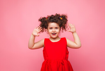 emotional portrait of a little girl in a red dress on a pink background.
