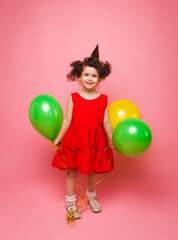Portrait of a cheerful little girl isolated on a pink background, holding a bunch of colorful balloons, posing.