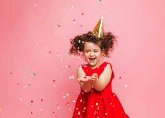 a little girl in a red dress celebrates her birthday, blowing and catching confetti on a pink...