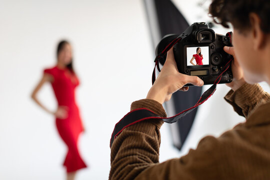Professional male photographer and beautiful female model in red dress making beauty or content photoshoot in studio