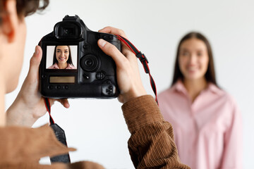 Photographer taking portrait of young beautiful woman in photostudio, focus on working digital camera during photoshoot - obrazy, fototapety, plakaty