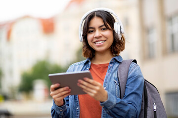 Smiling Arab Female Student In Wireless Headphones Using Digital Tablet Outdoors