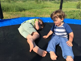 two brothers play and rest sit and lie on a trampoline the younger one shows his tongue