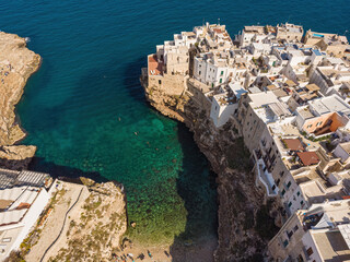 People bathing in the sun in Blue Lagoon, Polignano a Mare the beach. Aerial view of swimming in beautiful clear sea water. Top view from flying drone.