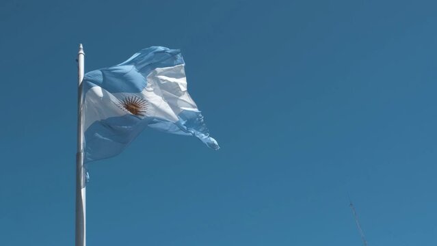 Argentine flag flying on a flagpole against a blue sky on a sunny day. Patriotic symbol of Argentina