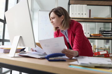 Focused woman reads accounting documents standing at table