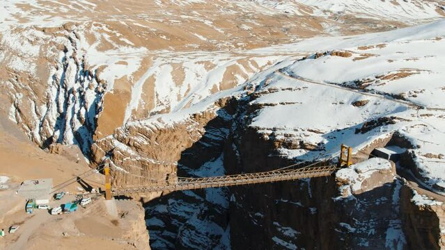 4K aerial view of Chicham bridge connecting Kibber and Chicham villages in Spiti Valley, India. Highest suspension bridge of Asia. 4,145 meters above sea. Bridge between two snow covered mountains