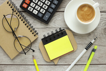 blank notepad and yellow sticker with coffee and calculator on wooden table, top view
