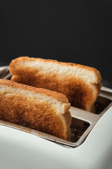 Close-up shot of slightly burnt white bread toasts sticking out of a toaster on the black background. Ready toasts with a dark  crust. Morning breakfast concept