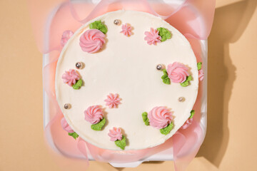 Small Korean style trendy bento cake decorated with pink cream cheese flowers in a white gift box on the beige background. Cake as a gift for a beloved one. Spring tender cake for a woman. Top view