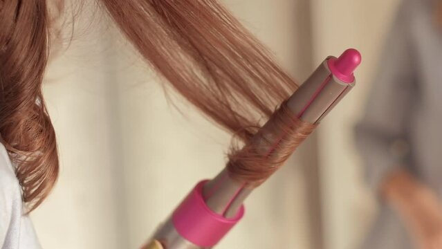 Brunette woman with wavy hair winding a strand of hair on pink curling iron