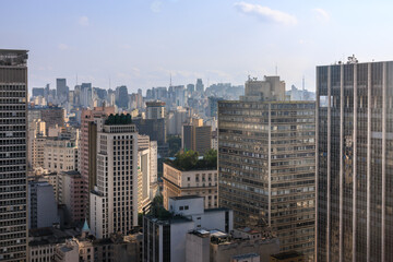 Região central da cidade de São Paulo vista do alto, com edifícios, torres antenas e céu azul com nuvens.