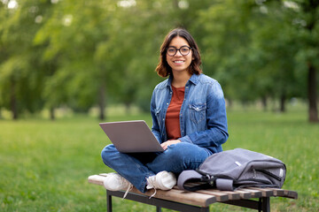 Smiling Arab Female Student In Eyeglasses Using Laptop Outdoors