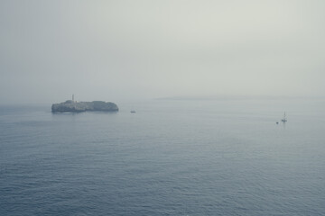 A view of a sea landscape with a small island in it during a foggy morning
