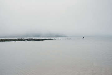 A foggy ocean landscape with a parent and a kid walking in the distance