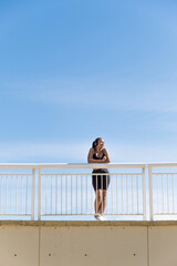 Active lifestyle: black latin woman listening to music with earphones in sportswear resting on white railing
