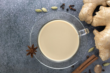 Indian masala tea in a transparent mug with spices - cinnamon, star anise, cloves, cardamom on a gray background.
