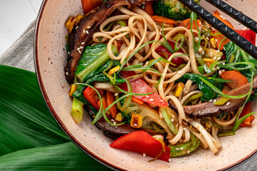 Udon stir fry noodles with beef meat and vegetables in a plate on white wooden background.